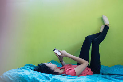 Full length of teenage girl using smart phone while lying on bed at home