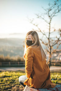 Midsection of woman sitting on field against sky