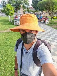 Portrait of a tourist with a medical mask, backpack, and camera taking a selfie with a cell phone