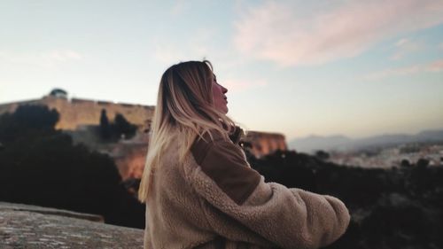 Side view of woman looking at city against sky