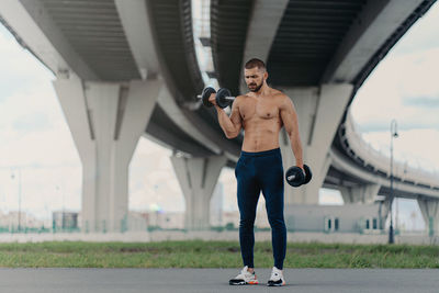 Full length of man lifting dumbbells on road