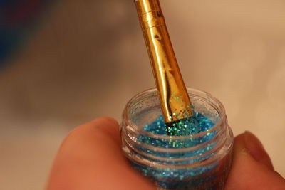 Cropped hand holding blue glitter in container