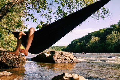 Low section of woman sitting on rock against sky