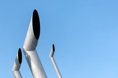 Low angle view of smoke stacks against clear blue sky