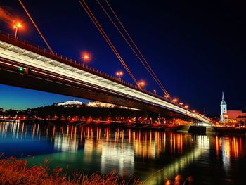 Illuminated bridge over river against sky at night