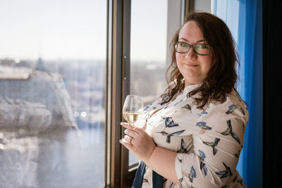 Large woman standing at the window with a glass of wine , the concept of loneliness