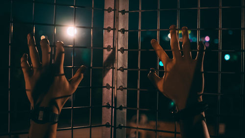 Cropped hands of man holding fence at night