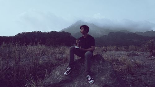 Man looking away while sitting on land against sky