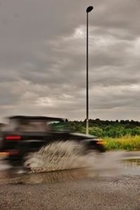 Cars moving on road against cloudy sky