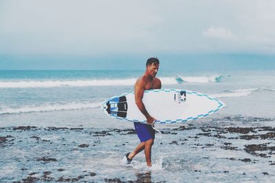 Full length of shirtless man standing on beach against sky