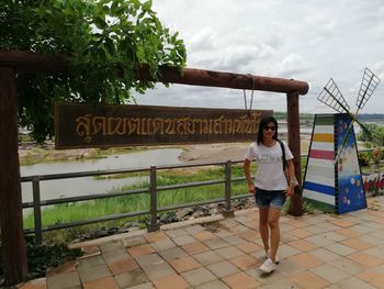 Full length portrait of young woman standing against sign