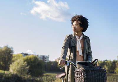 Thoughtful woman holding bicycle while standing on field