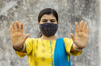 Indian woman showing open palm or stop gesture and looking at camera with nose mask on