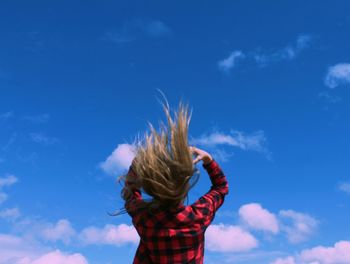 Low angle view of woman tossing hair against sky