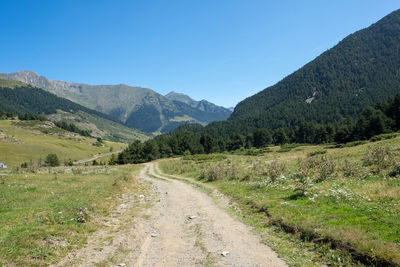 Dirt road by mountains against clear sky