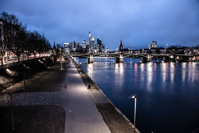 Illuminated buildings by river against sky in city