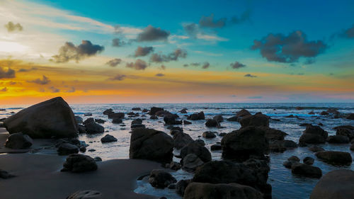 Rocks on beach against sky during sunset