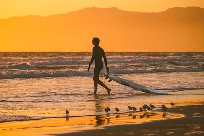 Full length of man on beach against sky during sunset