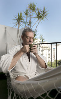 Full length of man drinking coffee while sitting outdoors