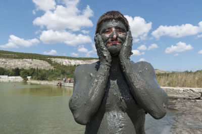 Portrait of man with mud on body standing against sea at beach