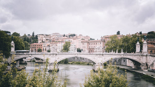 Bridge over river in city against cloudy sky