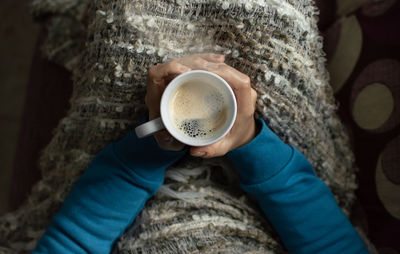 Directly above shot of woman holding coffee cup at home