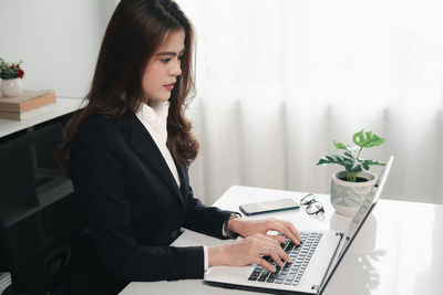 Young woman using mobile phone while sitting in laptop