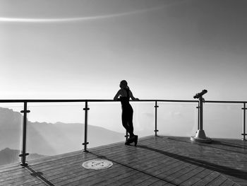 Rear view of woman standing by railing against clear sky