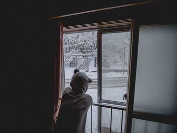 Rear view of woman looking through window during winter