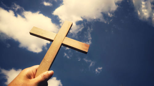 Low angle view of hand holding cross against sky