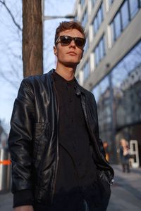 Portrait of young man wearing sunglasses standing against sky in city