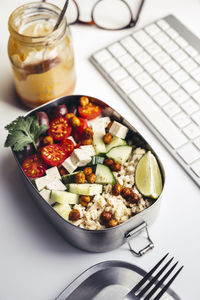 Lunch box with fresh vegan salad lying on desk in front of computer keyboard