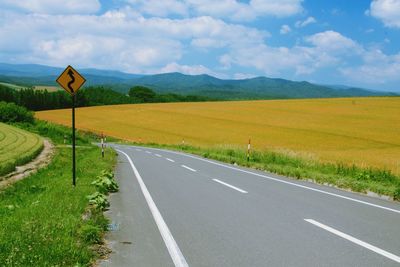 Road passing through field against cloudy sky