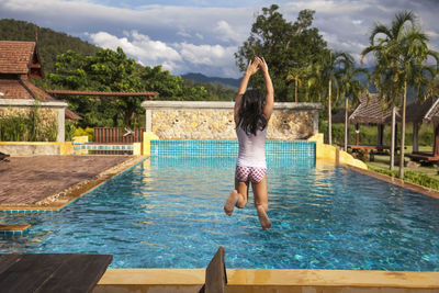 Girl jumping into swimming pool, thailand