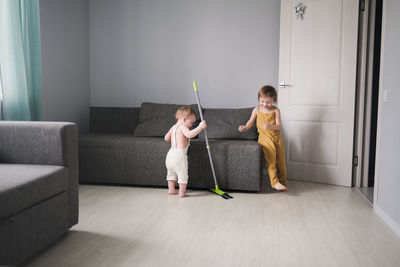 Baby 1 year old and older sister 3 years old with mop help mom clean living room with sofas