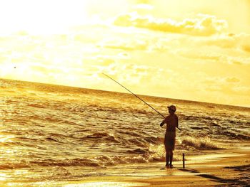 Man fishing in sea against sky during sunset