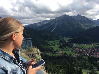 Woman using mobile phone over mountains against sky