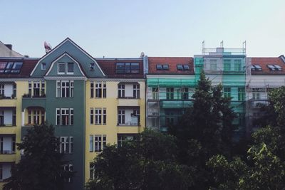 Trees by buildings in city against clear sky