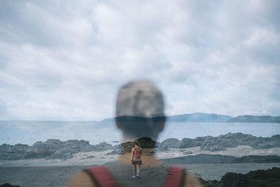 Rear view of man with arms outstretched against sea and sky