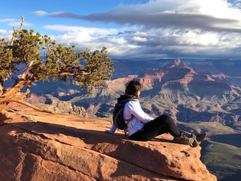 Man sitting on rock looking at mountains against sky