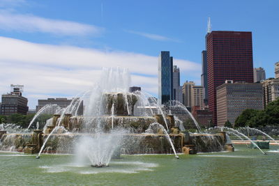 Fountain by buildings in city against sky