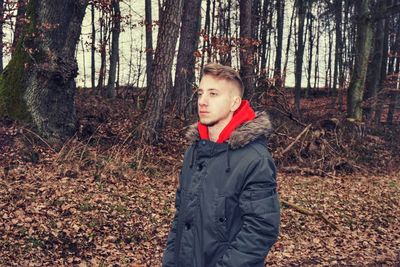 Young man looking away while standing in forest during autumn