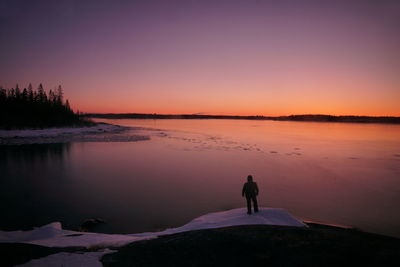 Rear view of silhouette woman standing at lakeshore during sunset