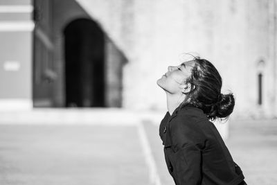 Side view of teenage girl standing against building with eyes closed in city