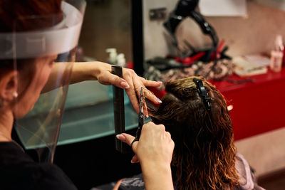 A close-up of a hairdresser cutting client's hair with a face shield