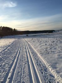 Tire tracks on snow field against sky during winter