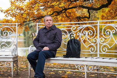Portrait of adult man. boarder sits on bench in park. rest, relaxation, slowdown in nature in autumn