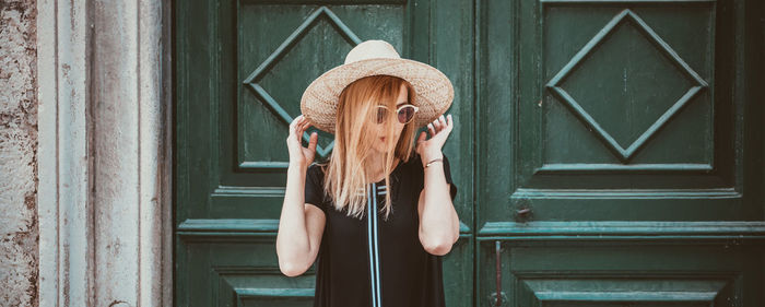 Young woman wearing hat while standing against doors