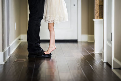 Low section of girl tiptoeing on father's feet at home