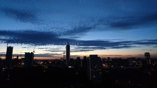 Silhouette of city against cloudy sky at dusk